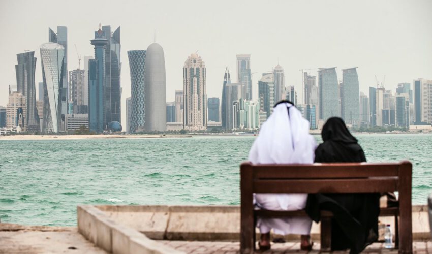 Asien, Arabische Halbinsel, Arabisch-Persischer Golf, Qatar, Katar, Doha: Skyline an der Promenade. Qatarisches Paar sitzt auf einer Bank am Wasser.

Engl.: Asia, Arabian Peninsula, Arabian-Persian Gulf, Qatar, Doha: Skyline at the corniche (promenade). Qatari couple sitting on a bank at the sea.

11-2013. buildings, sykscrapers, modern buildings, architecture, at sea, high-rise, tower block, port, harbour, harbor, people, couple, dishdasha, abaya, local, locals, traditional clothing, clothes, contrast.